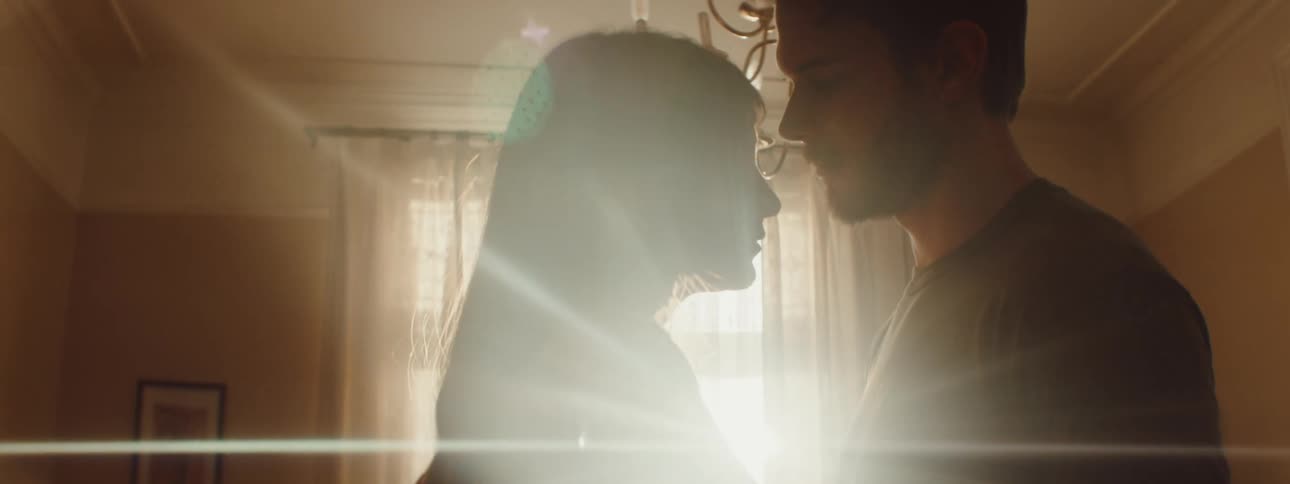 Man and woman looking at each other lovingly is silhouetted against the sunlight in the living room at home