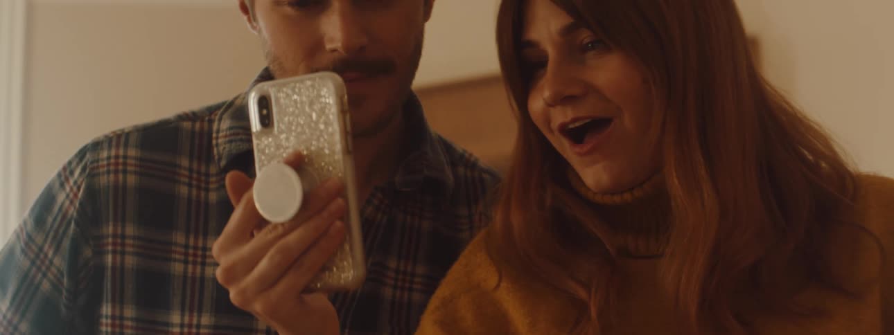 A man and woman talk and laugh as they look at a cell phone
