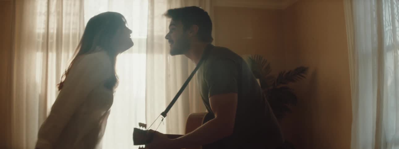 A husband is playing guitar for his wife indoors