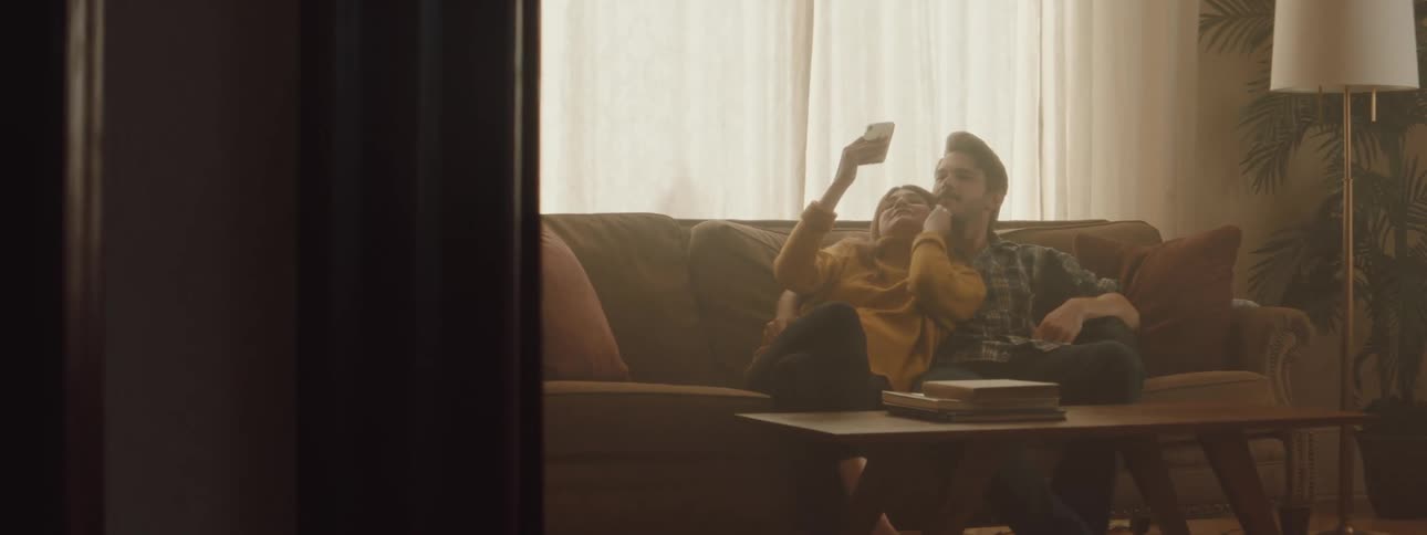Man and woman sitting on the couch take a selfie with a smartphone in the living room at home