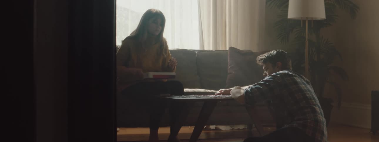 A man and a woman in a room playing with a puzzle with a wall and window in the background