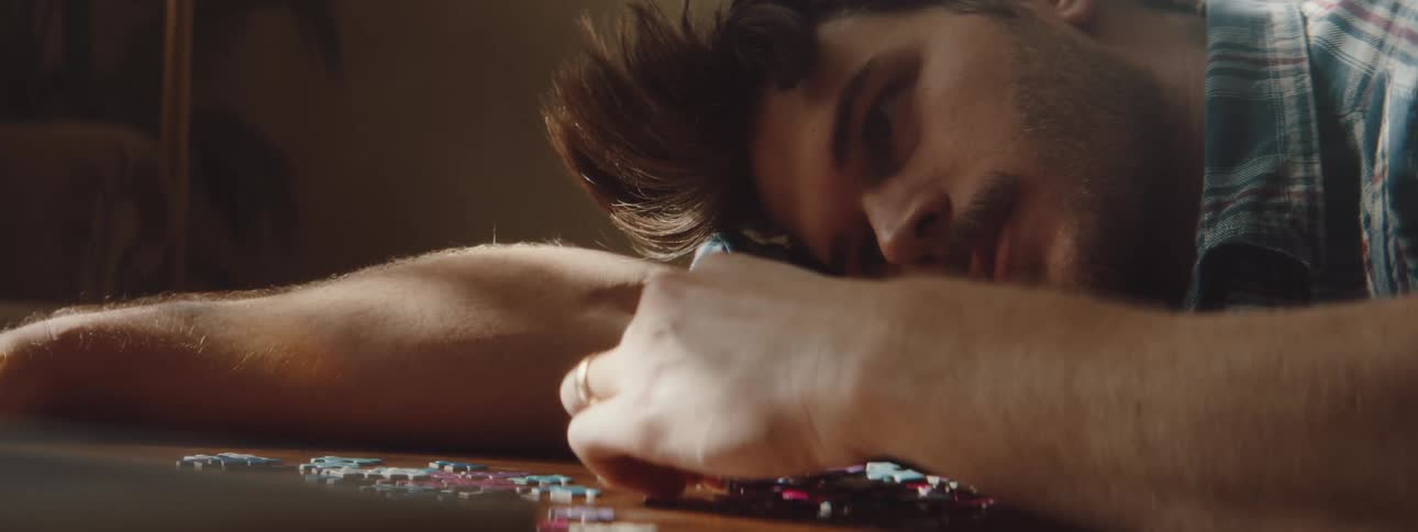 A man laying on a table playing with a puzzle with a couch and a wall in the background