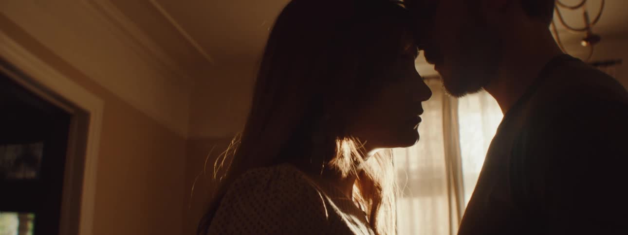 A man and a woman in a room hugging with a wall and window in the background
