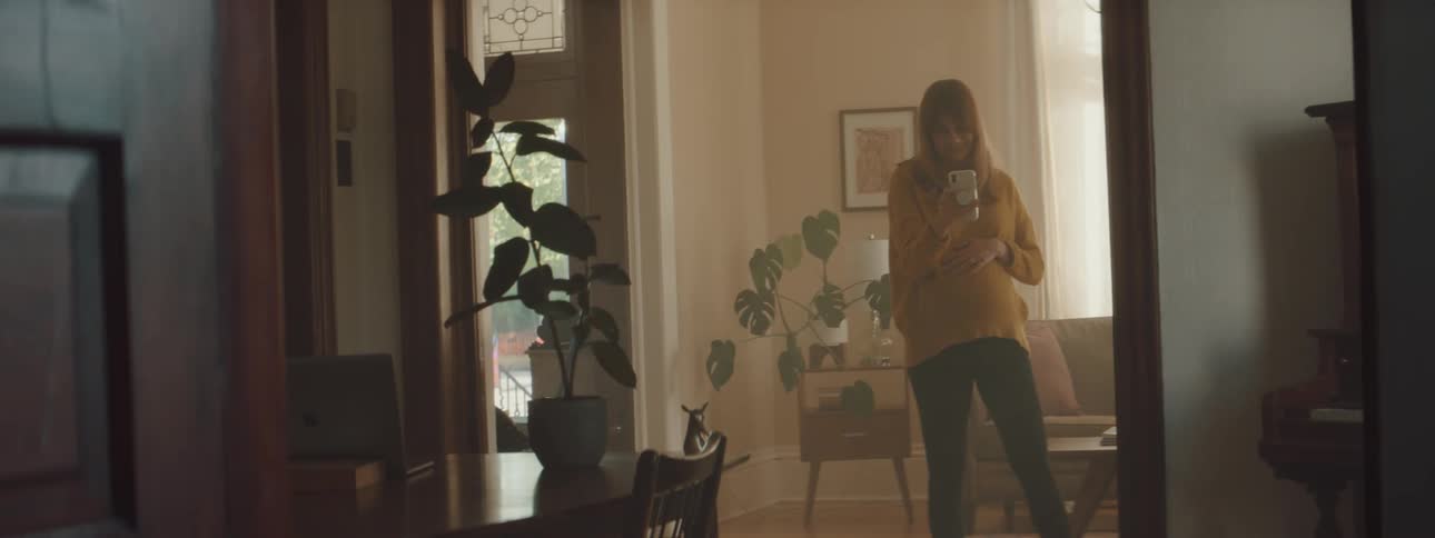 Young pregnant woman wearing yellow sweater talking on the phone in the living room