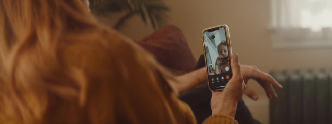 A woman in a room looking at a smart phone with a wall and window in the background