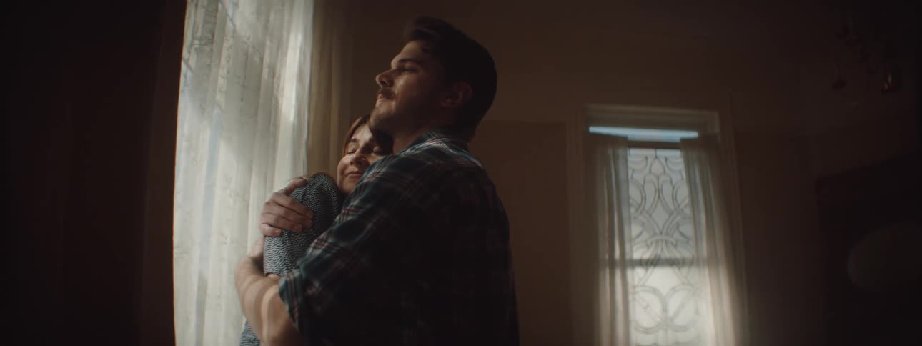 A man and woman hug as they look out a window in their home