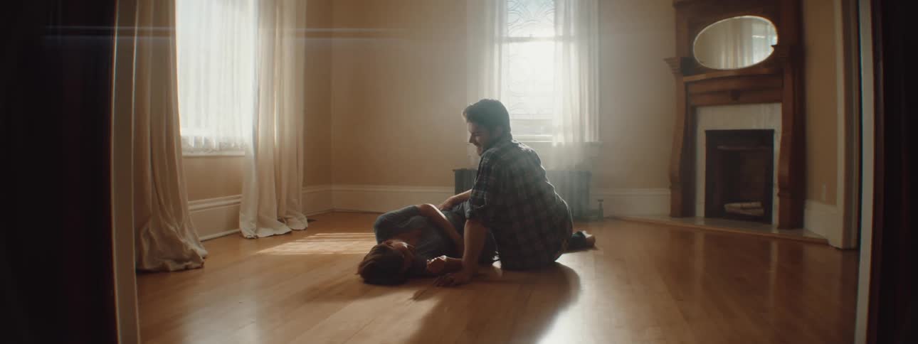 A husband and wife embrace on the wood floor of their empty living room