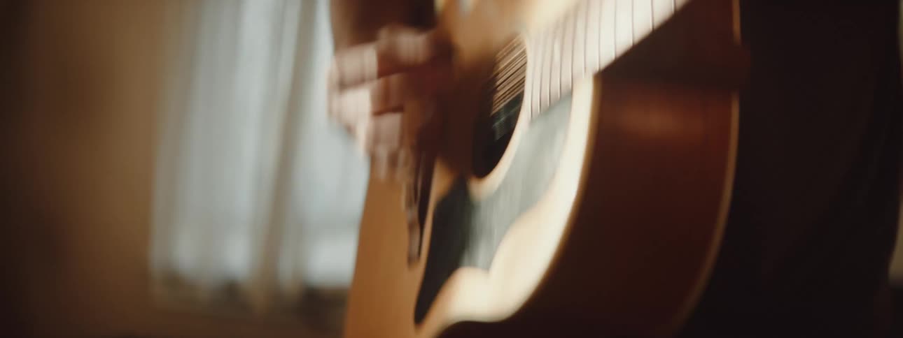 Man plays acoustic guitar in room under golden ceiling light fixture