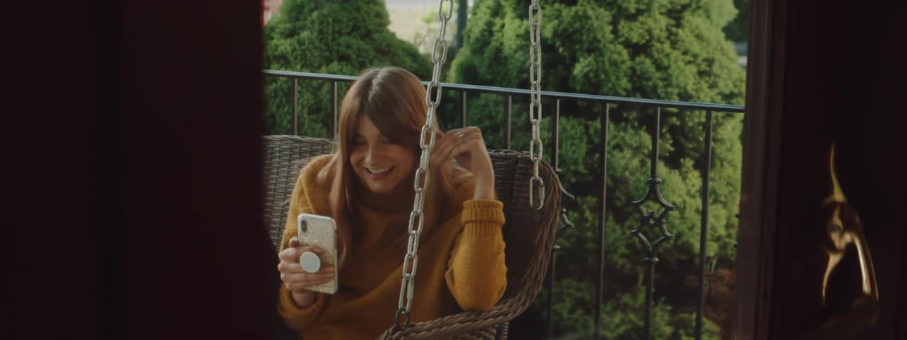 Woman sitting in swaying bench swing talks and waves at mobile phone