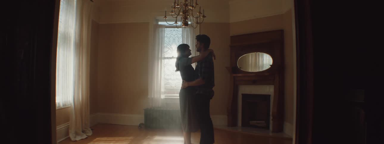 Man and woman cuddling each other lovingly are silhouetted against the window in the living room at home