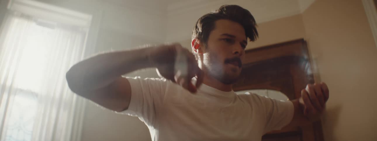 A man in a room stretching with a wall and window in the background