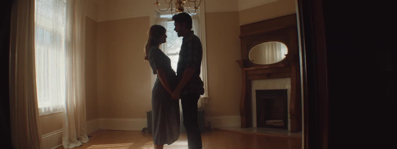 A man and a woman in a room hugging with a wall and window in the background