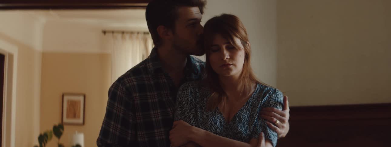A man walks up behind an woman and places his arms around her in a tight hug