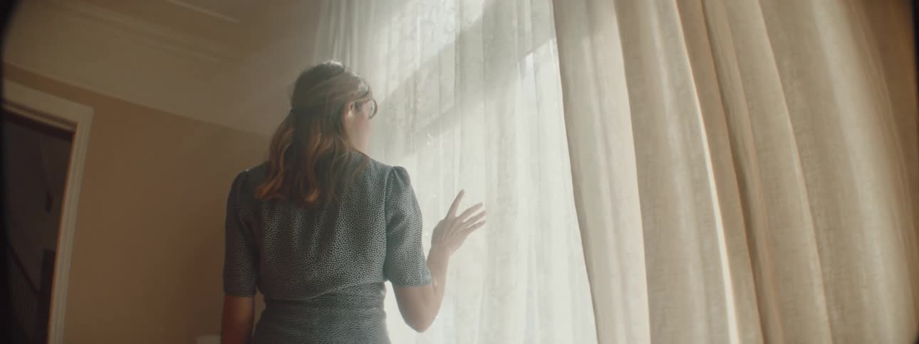 A woman checks the drapes in front of the window
