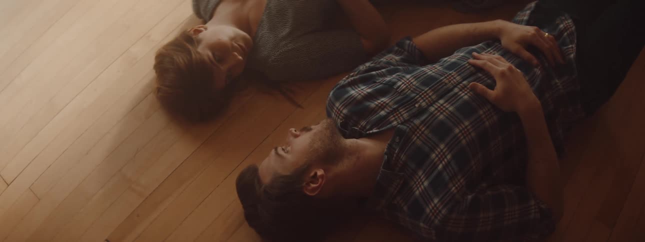Man and woman lying down on the floor looks into each others eyes lovingly in the living room at home