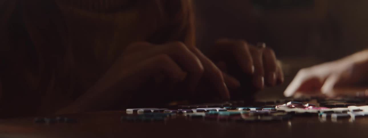A woman in a room playing with a puzzle on a table with a wall in the background