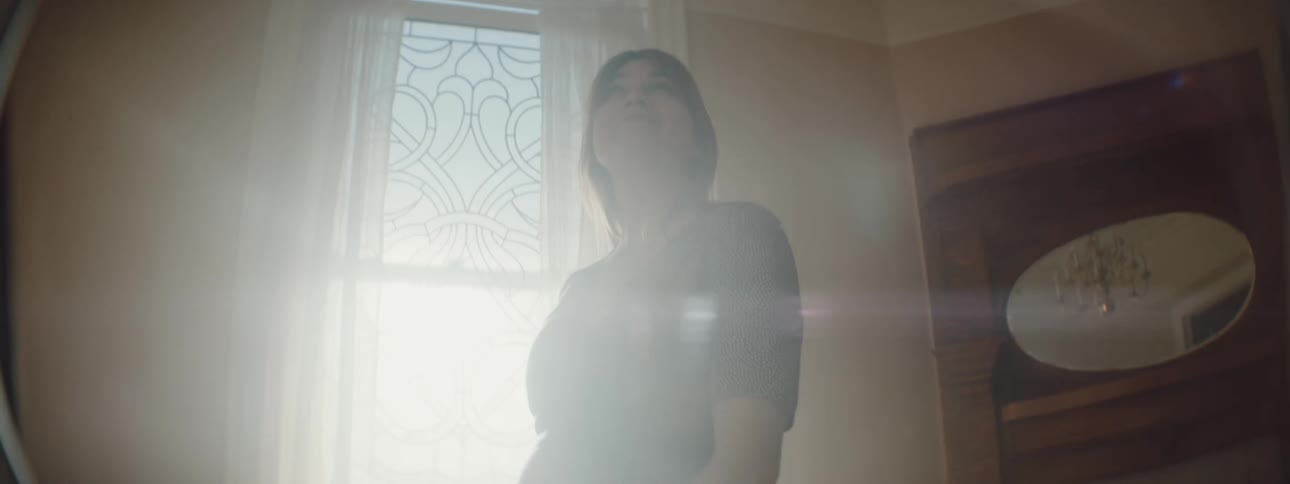 Woman with brown hair and a blue spotted dress turns around in a room