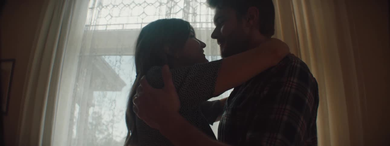 Man and woman cuddling and holding each other are silhouetted against the window in the living room at home