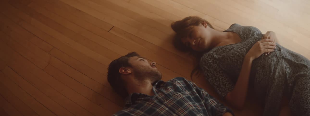 Man and woman lies down on the floor and looks into each others eye lovingly in the living room at home