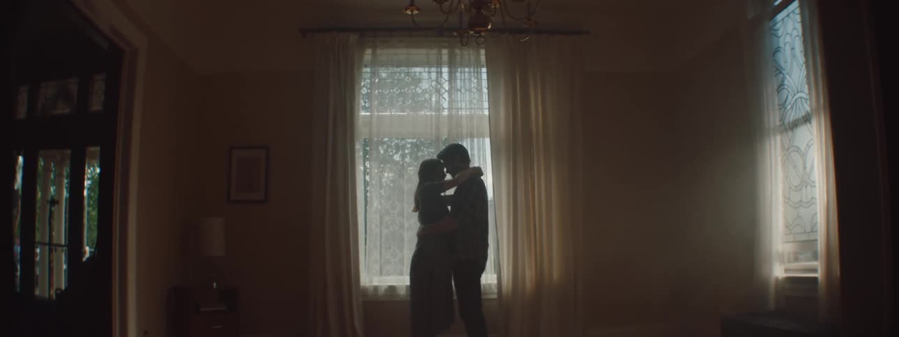 Man and woman cuddling each other lovingly are silhouetted against the window in the living room at home