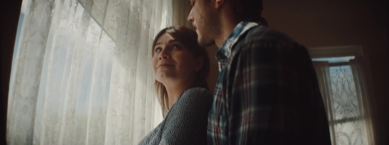 Husband and wife are standing in a house and looking out a window
