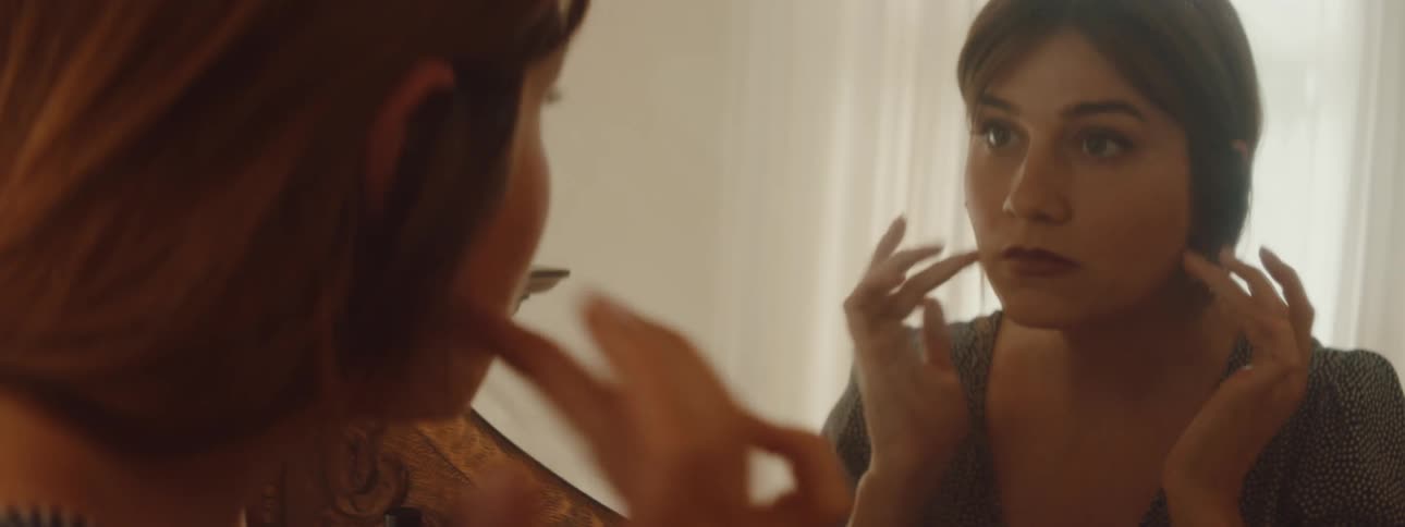 A caucasianfemale in a room looking at herself in a mirror rubbing her face