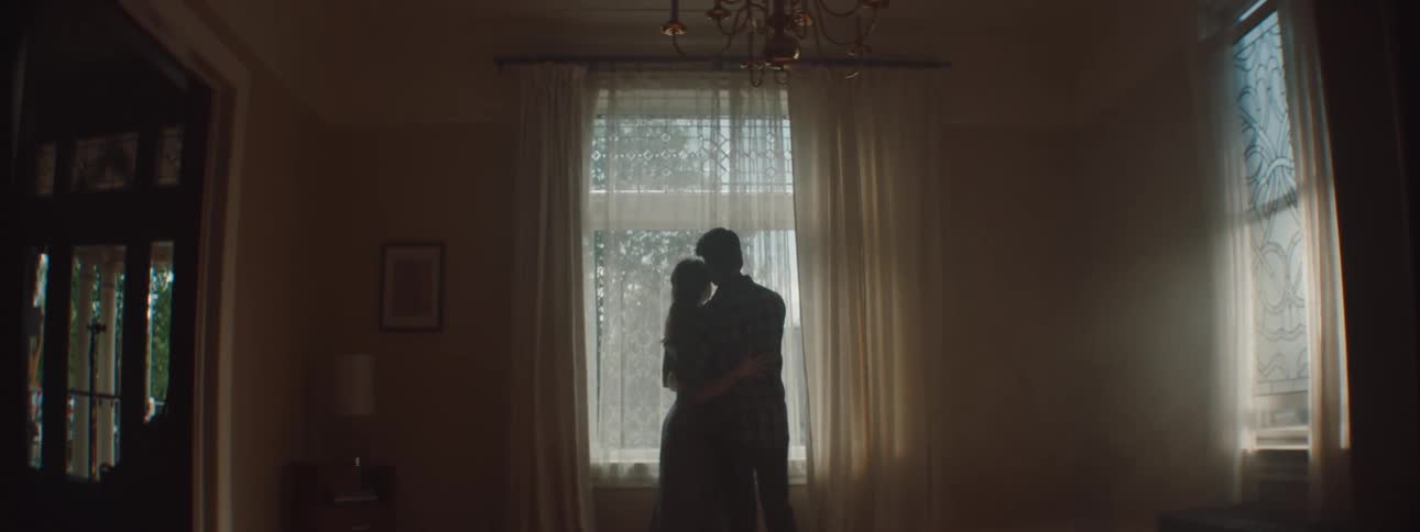 Young couple hugging in front of a window inside a dimly lit room
