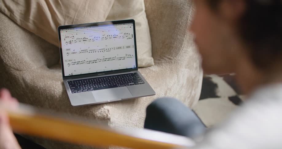A man looks at music notes on a laptop and plays his instrument
