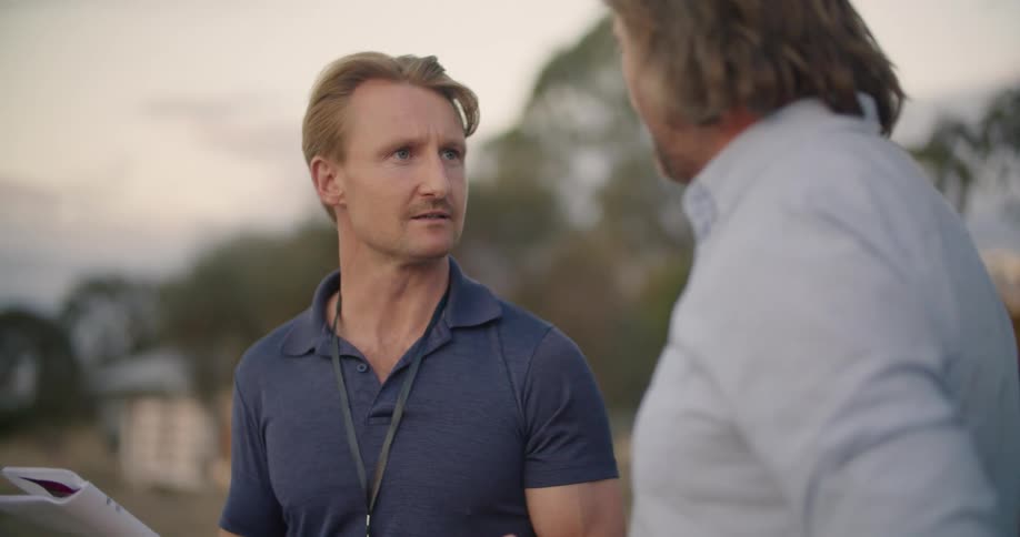 Two men are talking to each other outdoors at dusk