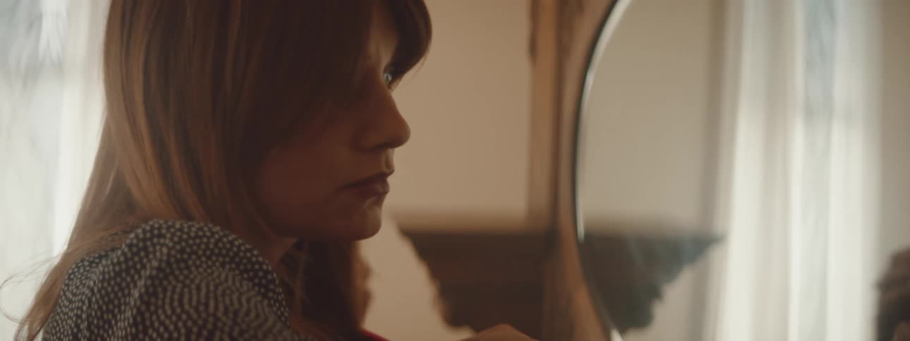 A woman is brushing her hair and looking into a mirror