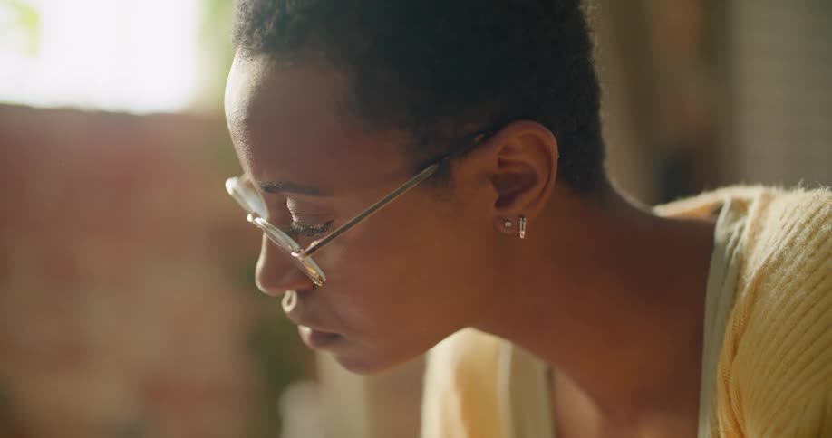 A woman is sitting inside of her house and wearing glasses