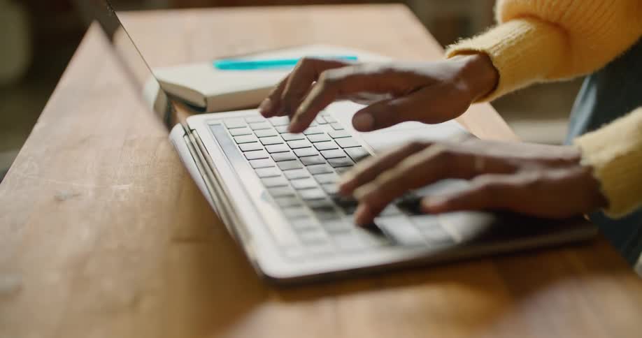 A black female at a desk in a shop typing on a laptop