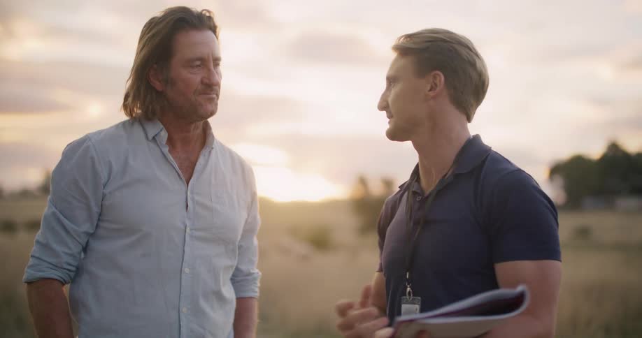 Two men talking on a field in the countryside shake hands at sunset