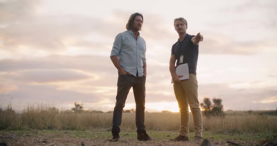 Two male friends are standing in a rural area talking to eachother