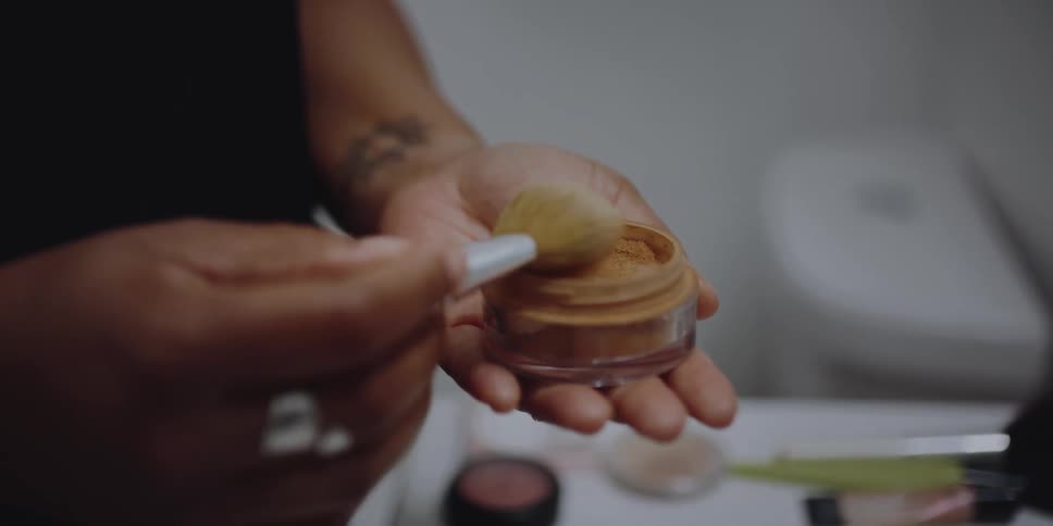 A woman dips a brush in to make up and then taps it