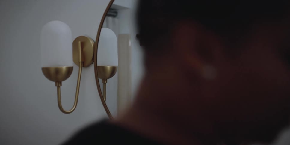 A man stares at her reflection in a bathroom mirror then walks away