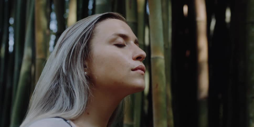A woman outside with her eyes closed with bamboo the sky and clouds in the background