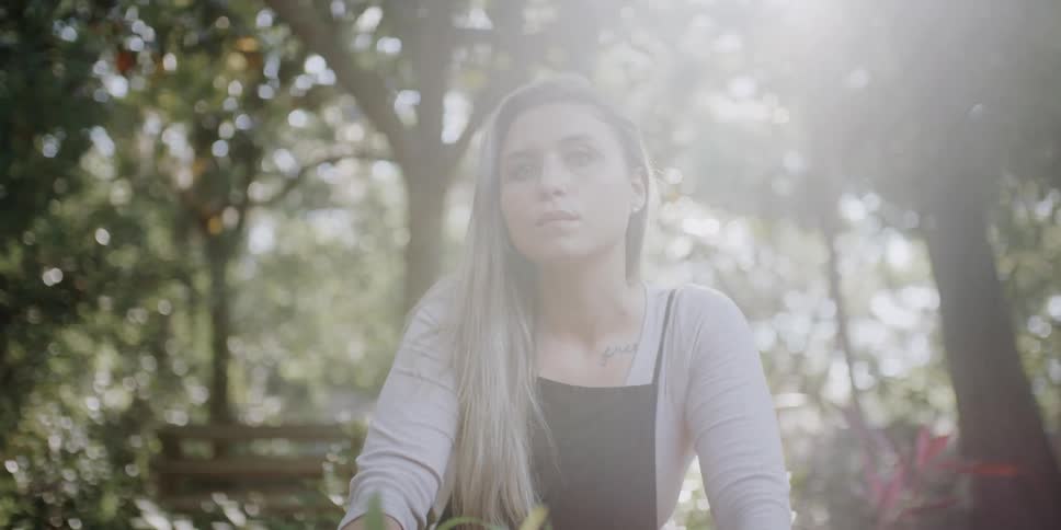 A woman sitting and staring with plants trees the sky and clouds in the background