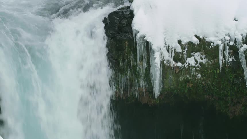 Tight shot of the lip of a waterfall and icicles in the heart of winter as the water rushes over the edge