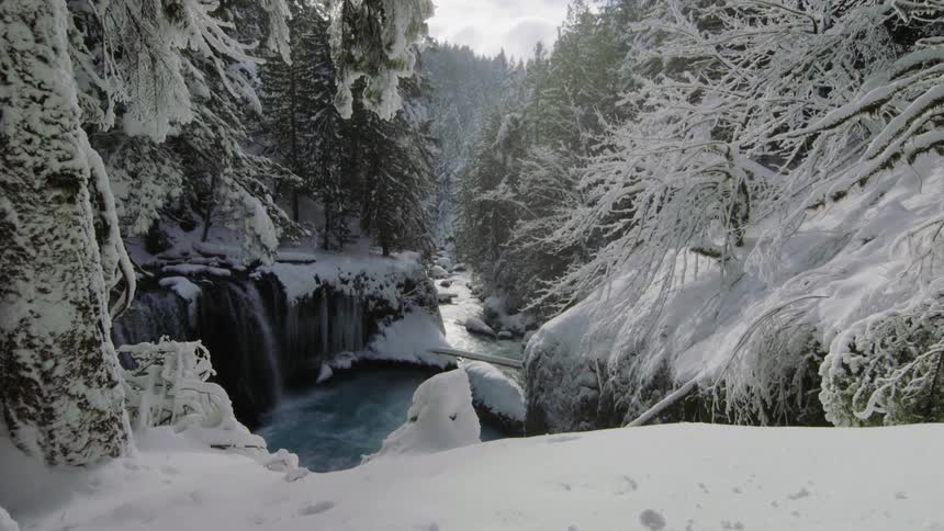 Hiker POV revealing an impossibly beautiful winter scene of snow covered trees, a blue pristine river and a clearing sky notched in the river valley