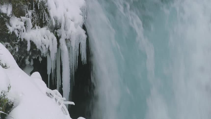 The large waterfall rages past the ice in this realtime shot of rushing water and icicles in the heart of winter