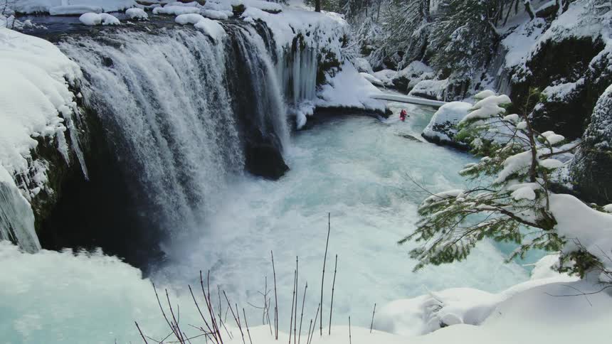 A massive waterfall and a whitewater kayaker in the middle of the winter as the kayaker paddles downstream towards another winter adventure