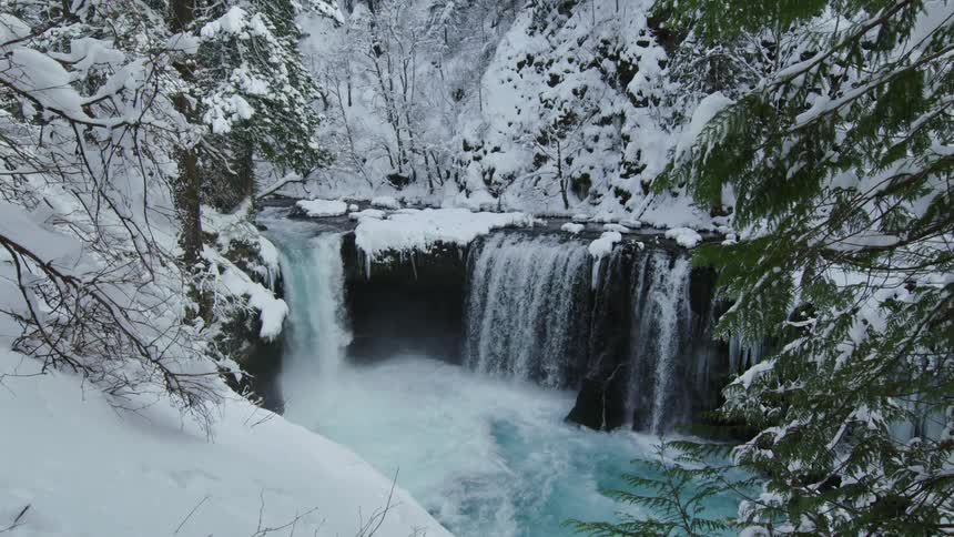 Slow motion tilt down of a an incredible winter river valley and waterfall after a massive dump of winter snow