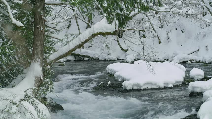 Static shot of a flowing river with feet upon feet of snow coating ever rock, tree and surface creating a winter wonderland