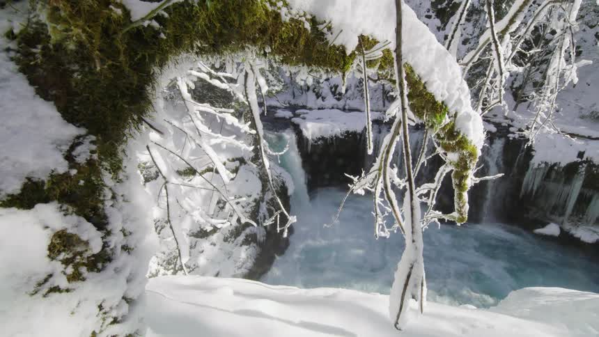 The camera lowers revealing a scene of winter magic and whitewater waterfalls with icicles and heavy snow