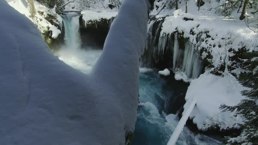 A v-shaped snow covered notch in a tree perfectly frames a giant snow covered waterfall in the heart of winter after a cold snap dumped feet of snow