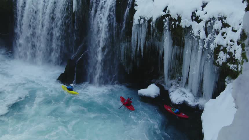 Three colorful whitewater kayaks paddling underneath frozen icicles and rushing whitewater after a heavy winter snow in the heart of winter just before Christmas Day