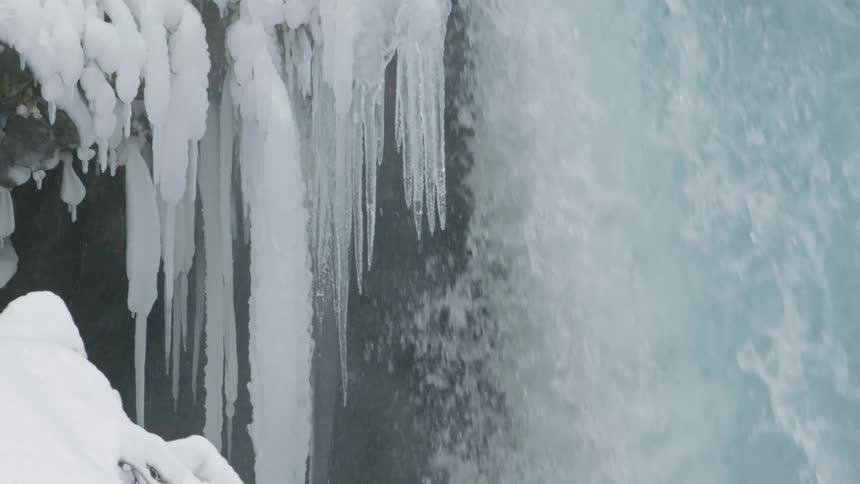 Epic static shot of icicles, water droplets and a cascading waterall in the middle of winter under a lot of snow