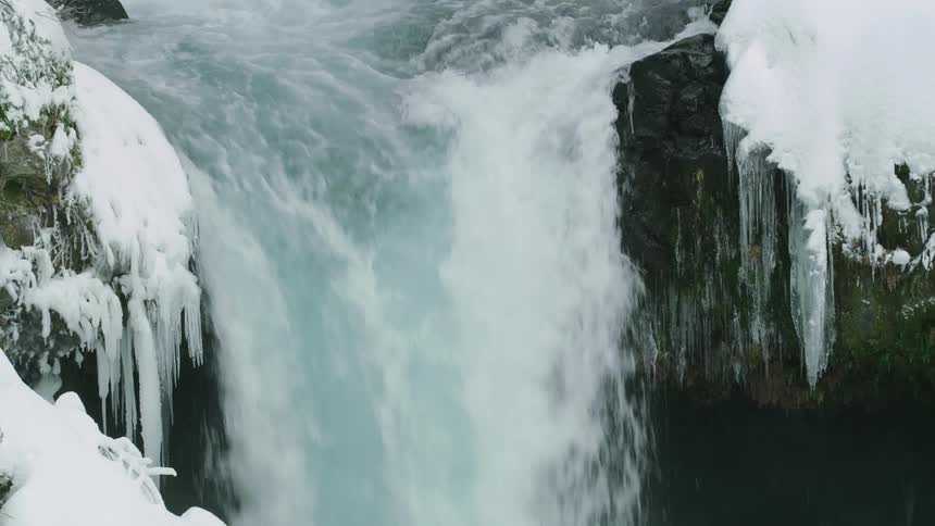 Real time shot of the top of a waterfall in winter with icicles on both sides as water cascades in the middle of the frame