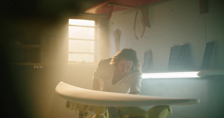 A man is sanding a surfboard in the shop